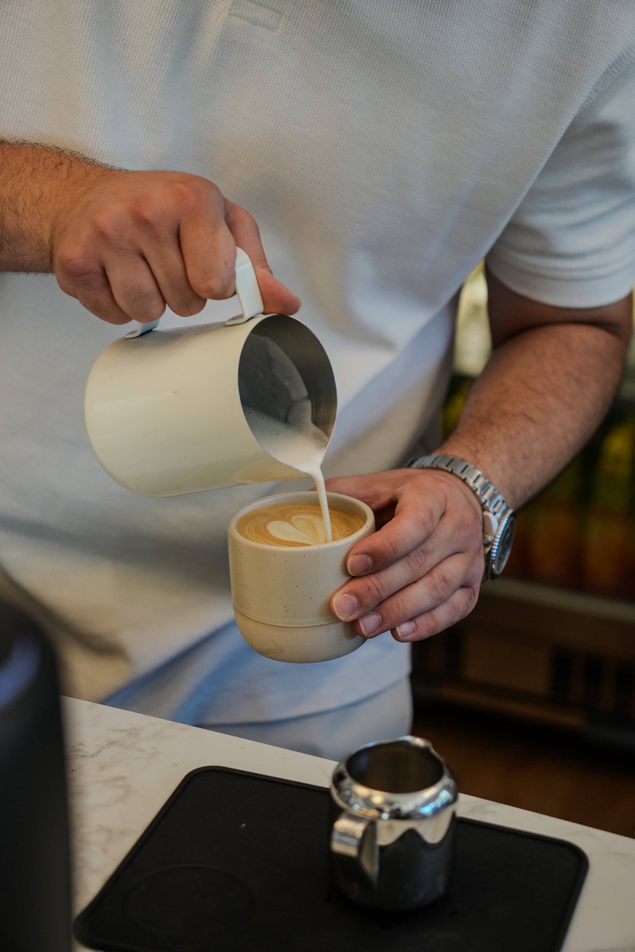 Milch wird aus einem Kännchen in einen Cappuccino gegossen