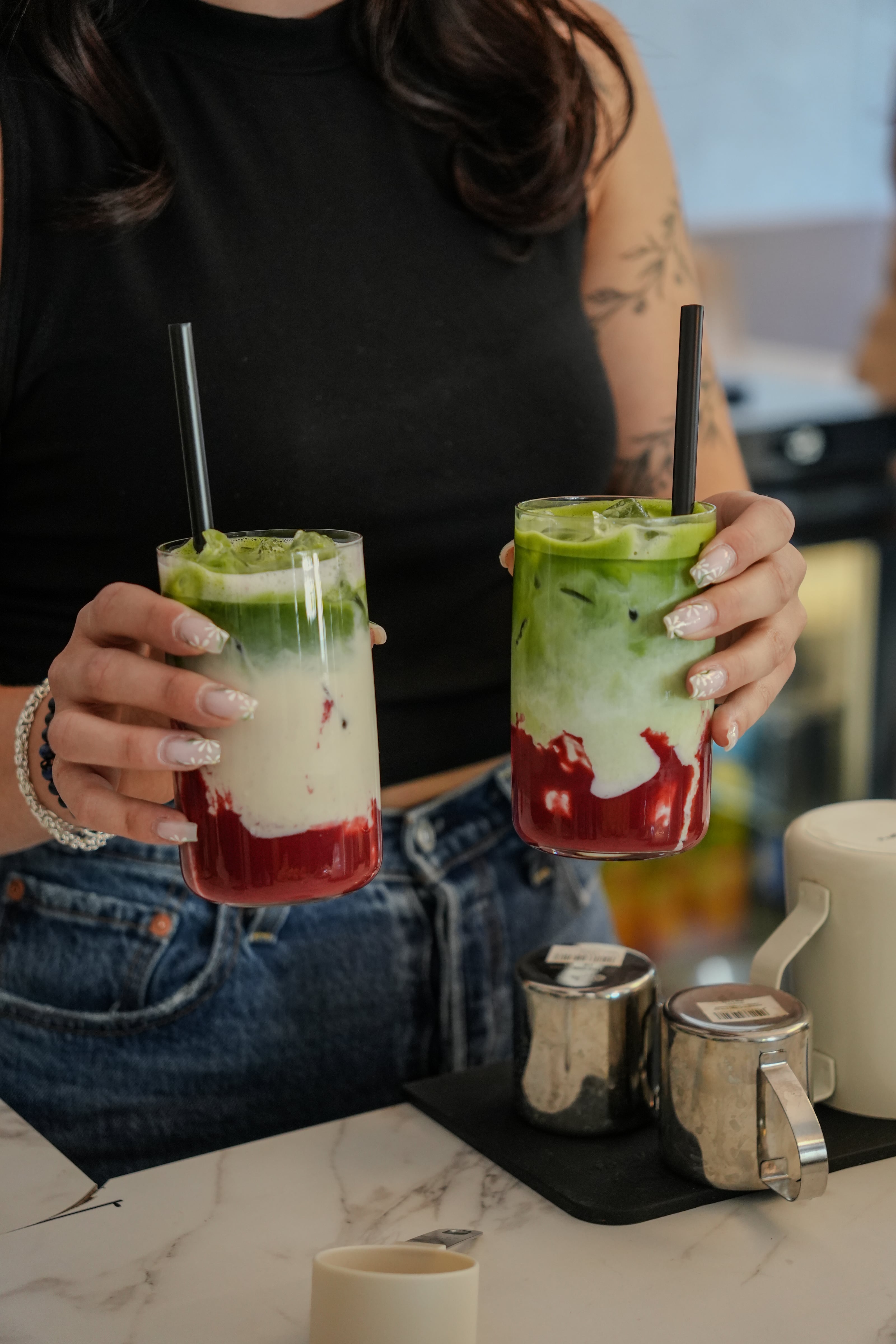 Zwei Iced Matcha mit Himbeere in Gläsern, am Tresen in den Händen gehalten