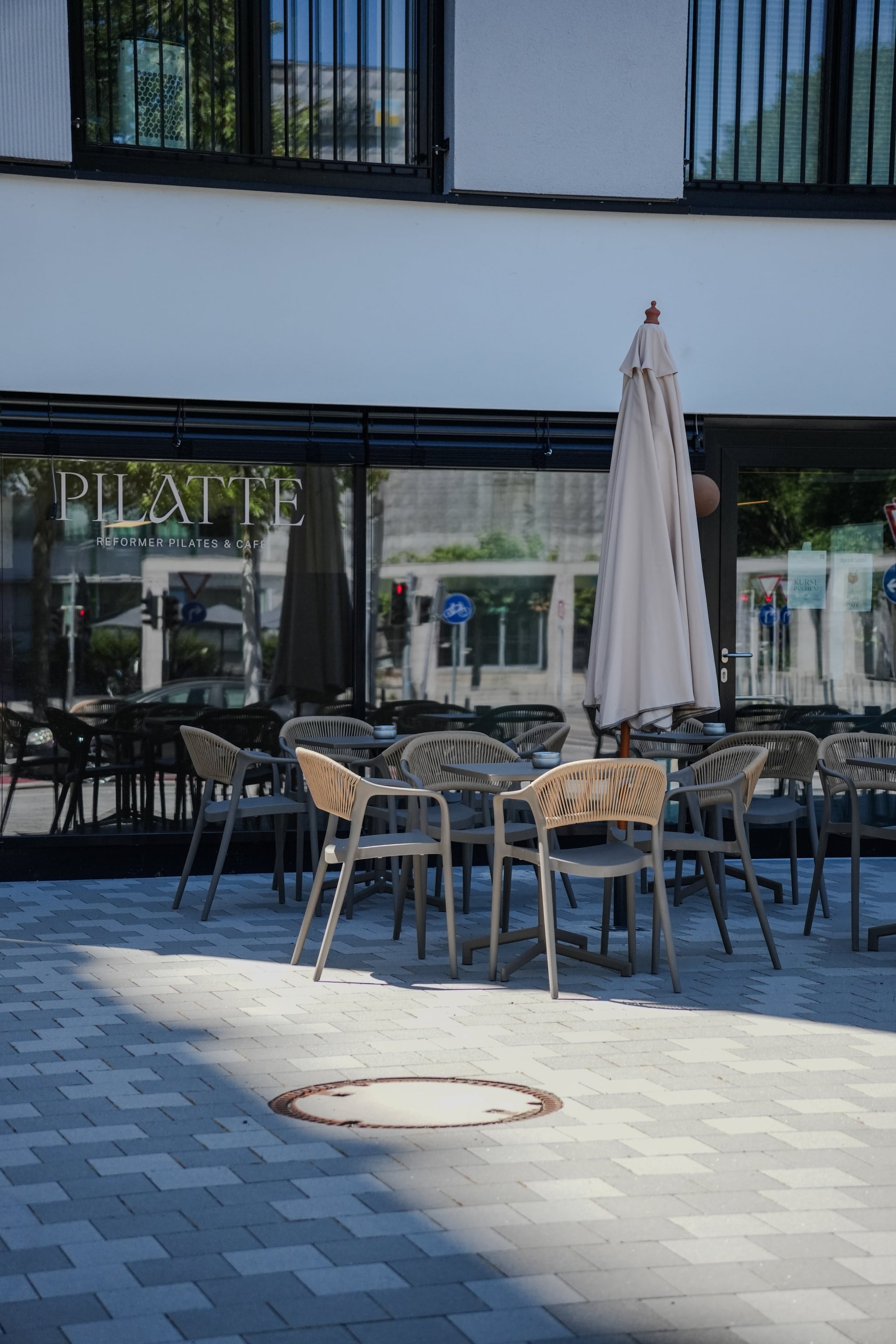Die Terrasse vor dem Café mit Stühlen und Sonnenschirm, im Schaufenster die Wortmarke